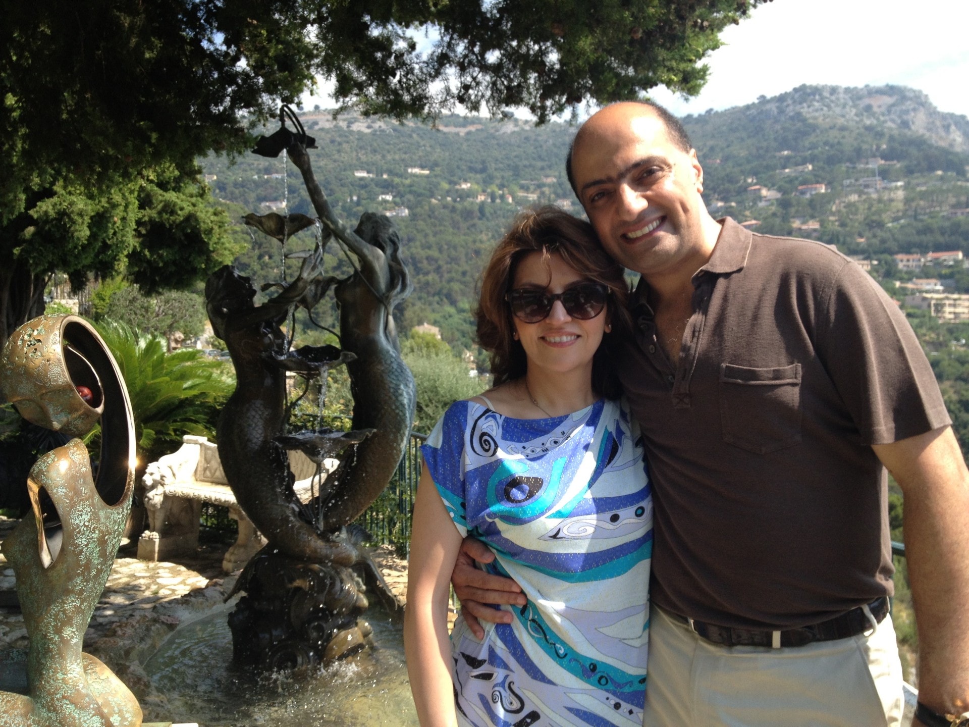 Dr. Hosein Khajeh-Hosseiny and a companion on a garden terrace beside a bronze mermaid fountain, with wooded hills behind